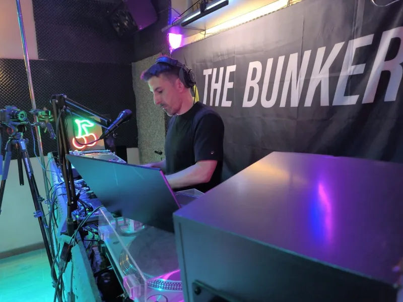 Un DJ mezclando con platos en el estudio, delante de la lona de The Bunker