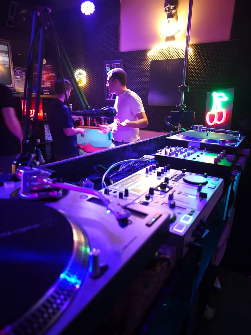 Platos y controladora en la cabina, con gente charlando al fondo del estudio
