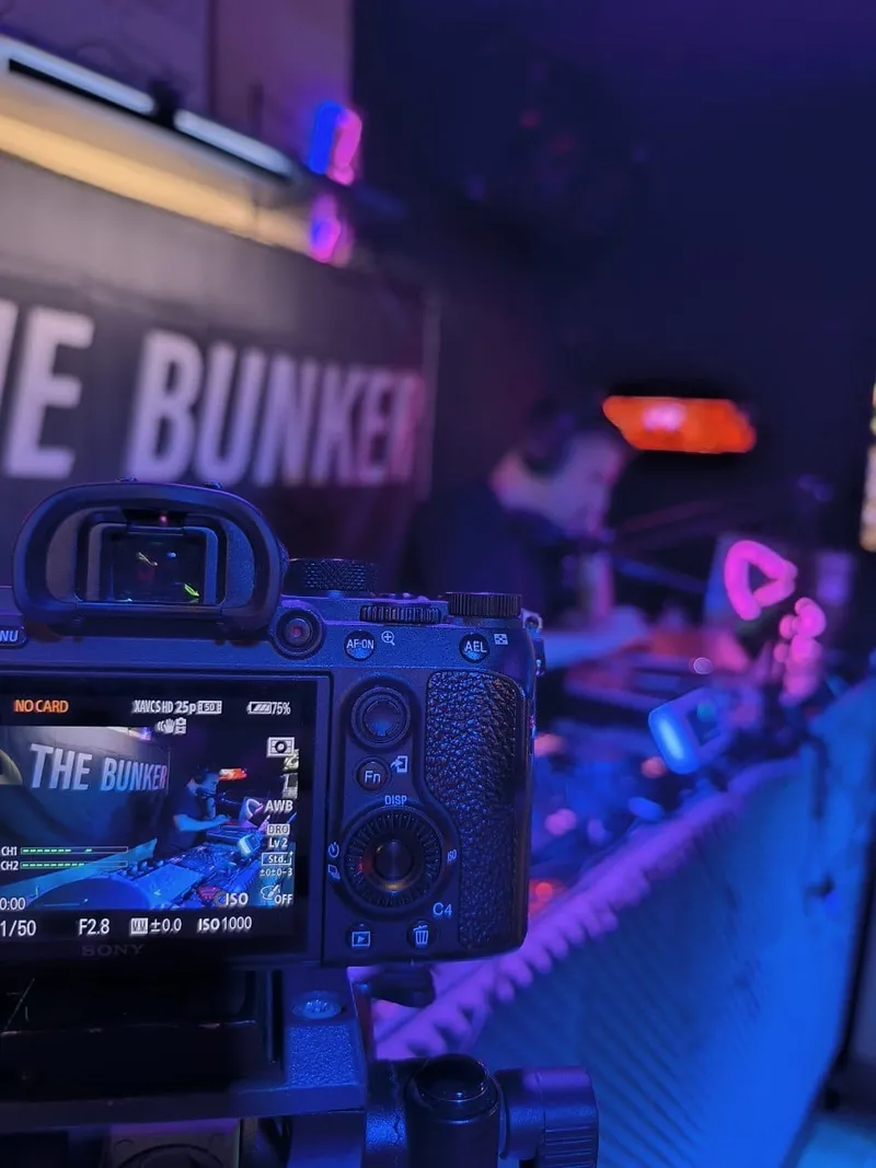 Primer plano de la cámara grabando un set, con la lona de The Bunker detrás