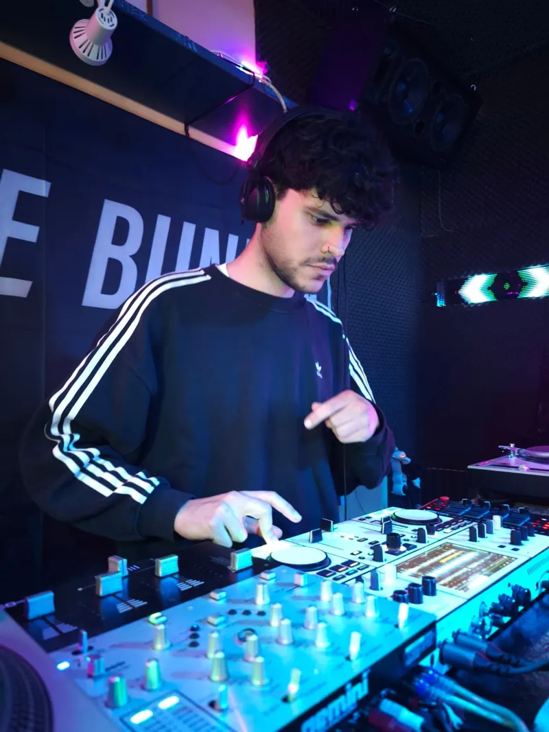 Un DJ con cascos pinchando en la controladora, delante de la lona de The Bunker
